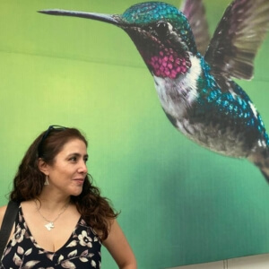 Lorena, professional travel concierge and local partner, posing in front of a vibrant green hummingbird mural during a cultural tour.